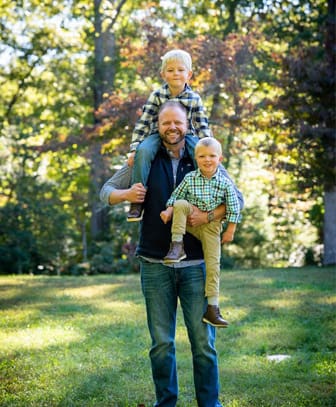 About Our Agency - Chad McKinney Standing Outside in the Backyard with his Two Sons on a Sunny Day